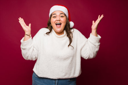 Overweight hispanic woman looking excited and surprised wearing a santa hat happy about the christmas holidaysの写真素材