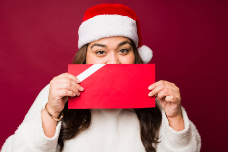 Portrait of a happy plus size woman with a santa hat receiving a red mock up gift card as a christmas presentの写真素材