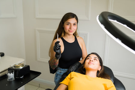 Happy young woman beautician smiling while using a blade during a microblading brow service in the beauty salonの写真素材