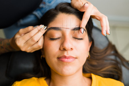 Attractive hispanic woman relaxing in the beauty room doing a brow design and hair removal service...