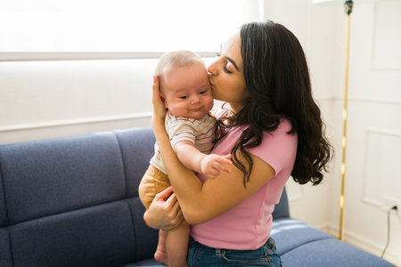 Caucasian beautiful mom hugging while carrying her newborn baby at home and kissing him feeling a...