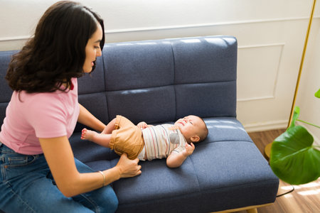 Loving mother sitting on the sofa and changing diaper and clothes for her crying upset newborn babyの写真素材