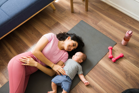 High angle of a cheerful mom in activewear working out at home and having fun with a workout while taking care of her newborn babyの写真素材