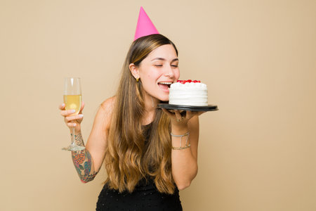 Cheerful beautiful woman eating delicious birthday cake and drinking champagne and alcohol celebrating having funの写真素材