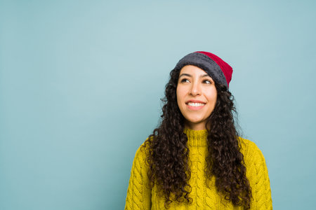 Attractive latin young woman with a knit hat wearing a yellow sweater and thinking about the cold winter weather with copy space adの写真素材