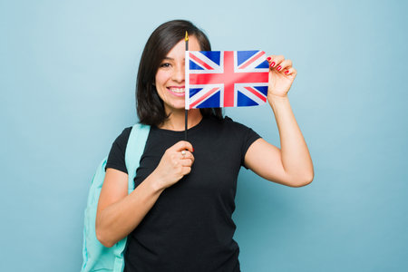 Happy caucasian woman in her 30s smiling taking English lessons smiling in front of a blue background showing a UK flagの写真素材