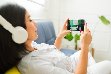 Rear view of a caucasian woman relaxing on the couch with headphones watching a streaming video...