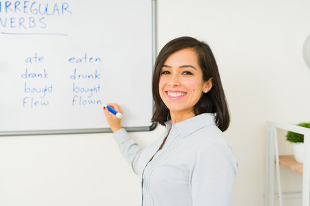 Happy attractive woman smiling while writing on the whiteboard teaching an English lesson to the...