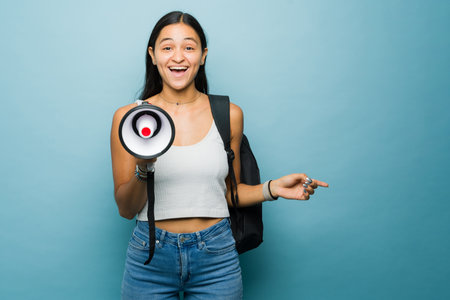 Excited young woman and happy student using a megaphone to give a college university message...