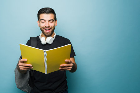 Surprised happy young man and student reading a book and studying for university while excited next...
