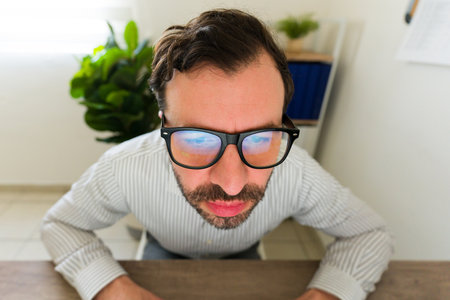 Attractive hispanic man and boss using glasses typing on the computer and looking at the screen from a wide angleの写真素材