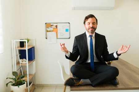 Relaxed businessman with a suit sitting at the desk doing a relaxing meditation while working at the officeの写真素材