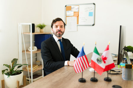 Caucasian politician diplomat with a suit sitting at his office desk with Mexico, US and Canada flag...
