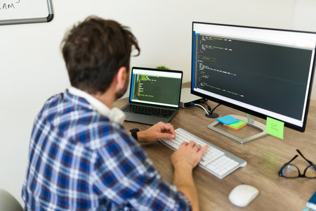 Hispanic programmer typing and writing a new code on the computer while working at the office coding...