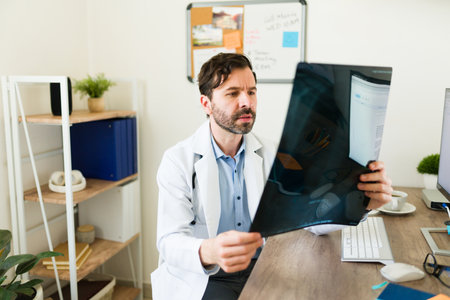 Handsome orthopedic doctor looking at the medical x-rays of a patient with a broken bone while...