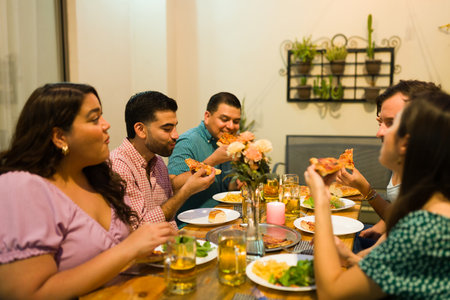 Beautiful happy friends talking and having fun while eating pizza during dinner in the backyard having a celebrationの写真素材
