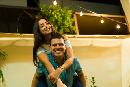Attractive happy couple in the backyard at night having fun doing a piggyback while smiling making eye contactの写真素材