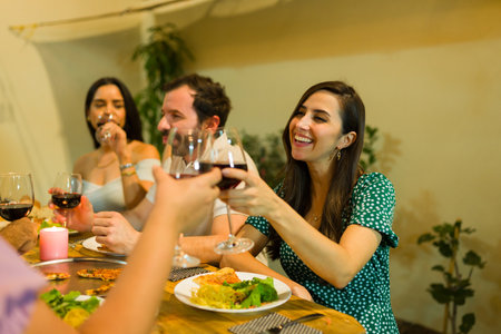 Smiling young women and men laughing having a toast drinking wine together after eating dinner...