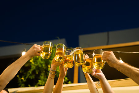 Close up of a group of young people making a toast with beers and celebrating friendship during a partyの写真素材