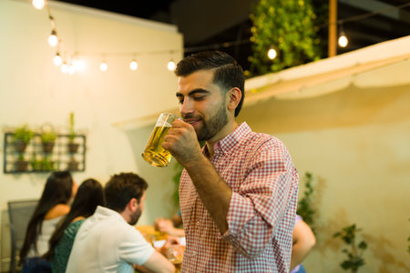 Mexican young man smiling while having fun with his friends at night while drinking beerの写真素材