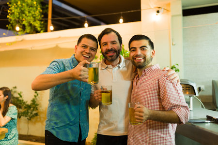 Portrait of happy men friends smiling and saying cheers while making a toast drinking beer together during a dinner in the backyardの写真素材