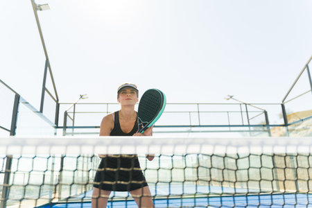 Beautiful happy woman having fun smiling while playing a match on the court holding a padel racketの写真素材
