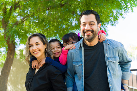 Happy beautiful caucasian family with two kids piggybacking while having fun together in the park smiling looking at the cameraの写真素材