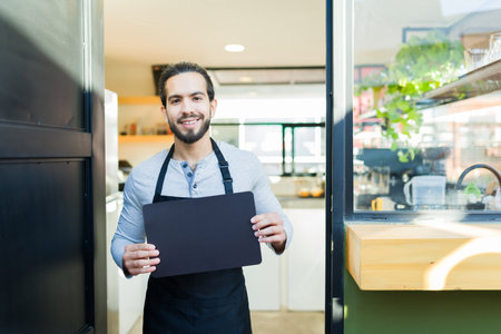 Smiling handsome barista worker showing the cafe menu with copy space and smiling making eye contact...