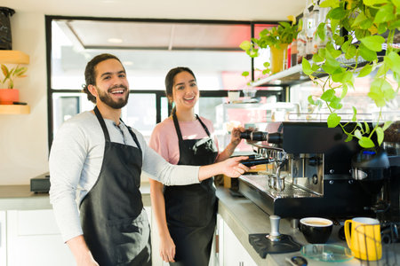 Cheerful couple of baristas laughing and having fun while preparing drinks at the coffee shop and using the coffee machineの写真素材