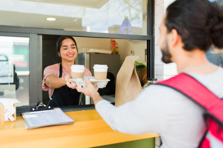 Happy woman worker handing the food and coffee order to the delivery person at the cafe restaurantの写真素材