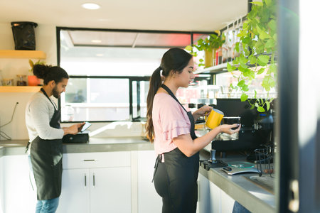 Young woman making a cappuccino drink while working together with a male barista at the coffee shop