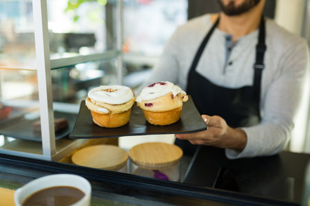 Hispanic male barista handing dessert pastry to a customer while working at the coffee shopの写真素材