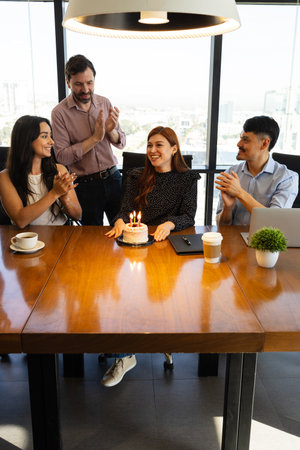 Beautiful woman with a birthday cake getting a nice celebration from her coworkers in an officeの写真素材