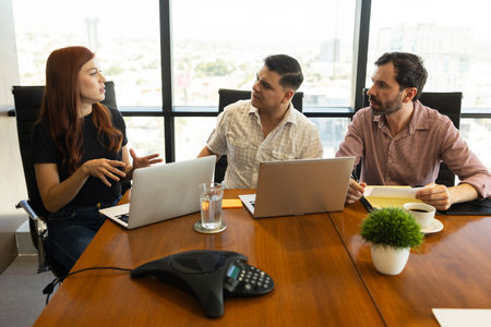 Team of businesspeople in casual clothing using laptop computers and having a discussion in a meeting roomの写真素材