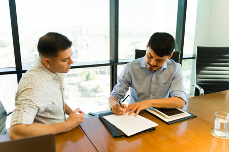 Portrait of a Latin man in casual clothing signing an agreement and closing a deal in an office