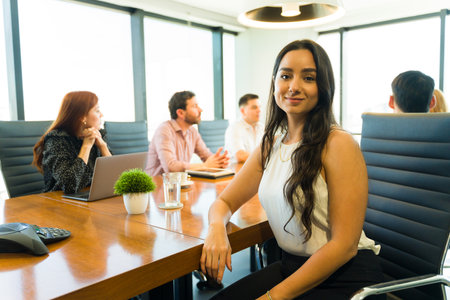 Pretty businesswoman in casual clothing sitting in a meeting room with other colleagues and making eye contactの写真素材