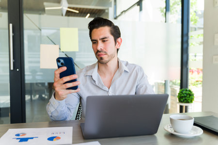 Portrait of a good looking businessman checking his messages on a smartphone in his office