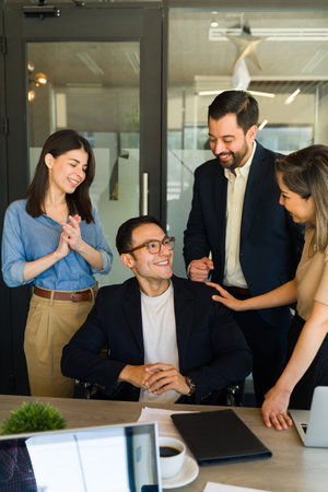Successful man in a wheelchair getting words of encouragement and recognition from his coworkersの写真素材