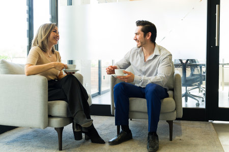 Good looking business partners having a chat and enjoying a cup of coffee together at an officeの写真素材