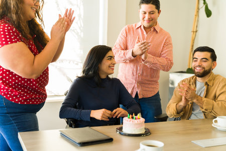 Happy businesswoman in a wheelchair getting a birthday cake and celebration in an officeの写真素材