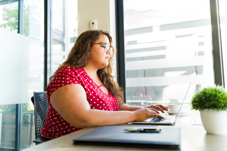 Pretty Latin fat woman wearing glasses and working on a laptop computer in a meeting roomの写真素材