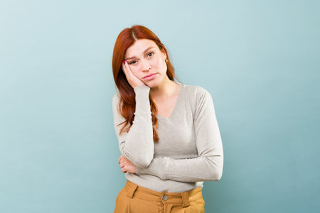 Tired sad caucasian redhead woman in her 30s looking exhausted and bored against a blue background