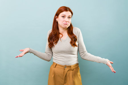 Redhead caucasian woman in a blue background shrugging her shoulders with no answer to a question
