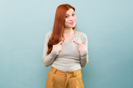Happy beautiful caucasian redhead woman pointing to herself and smiling making eye contactの写真素材