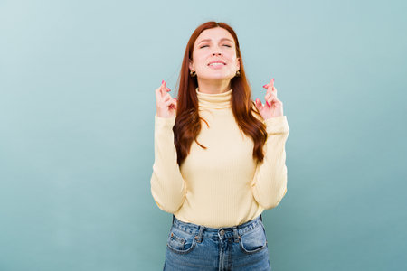 Caucasian beautifulr redhead woman crossing her fingers and asking for luck for her wish and dreams to come trueの写真素材