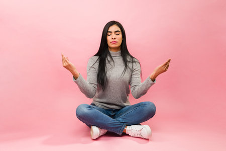 Relaxed latin woman living a stress free life doing meditation and breathing exercises against a pink backgroundの写真素材