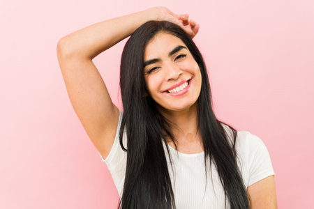Cheerful beautiful young woman smiling looking happy with an arm above her head feeling sexy looking at the cameraの写真素材