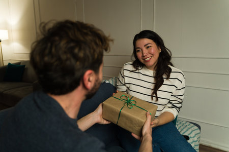 Beautiful asian woman receiving an anniversary present from her boyfriend while relaxing together at homeの写真素材
