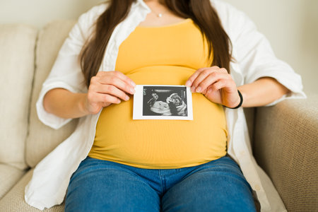 Close up of pregnant mother showing the ultrasound scan of her baby on her beautiful belly while at...