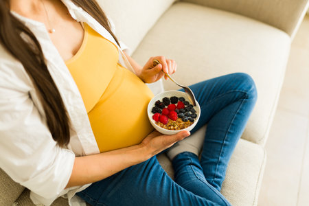 Top view of a healthy pregnant woman sitting on the couch while eating berries yogurt and healthy food during her pregnancyの写真素材